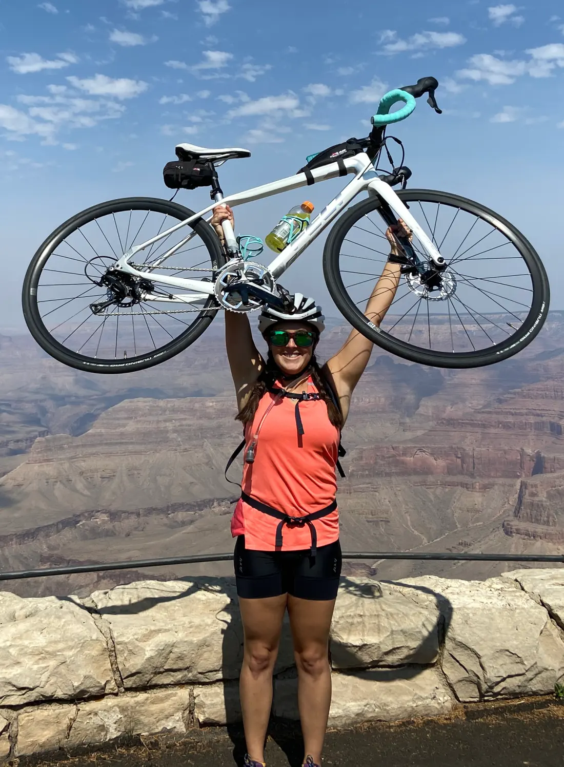 Ashley in cycling gear holding a bicycle overhead at the Grand Canyon